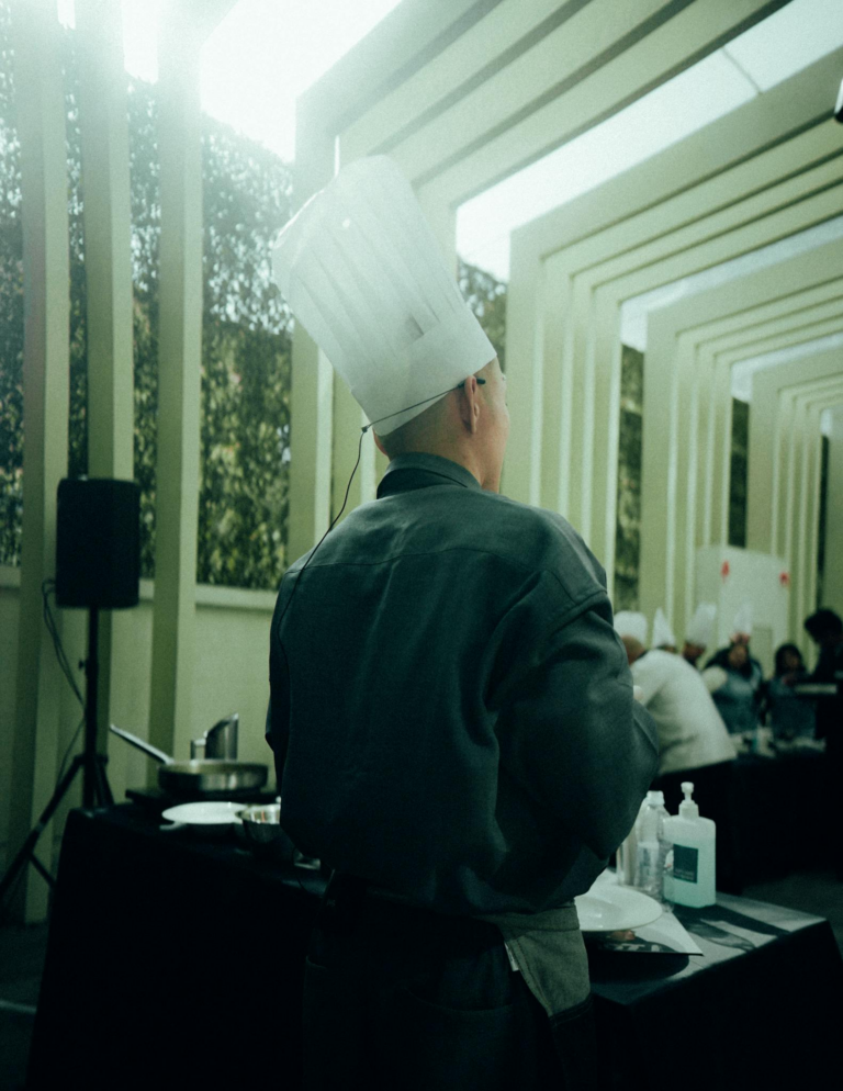 Chef wearing a hat preparing for a culinary demo. Focus on the back view in a professional setting.